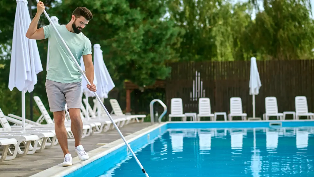 Pool maintenance worker skimming debris from water to prevent pool flu and maintain cleanliness