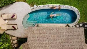 Aerial view of a man relaxing in a swimming pool, floating on his back with arms outstretched.
