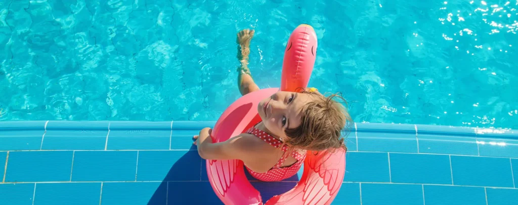 Little girl floating on pink flamingo in a chemically balanced pool