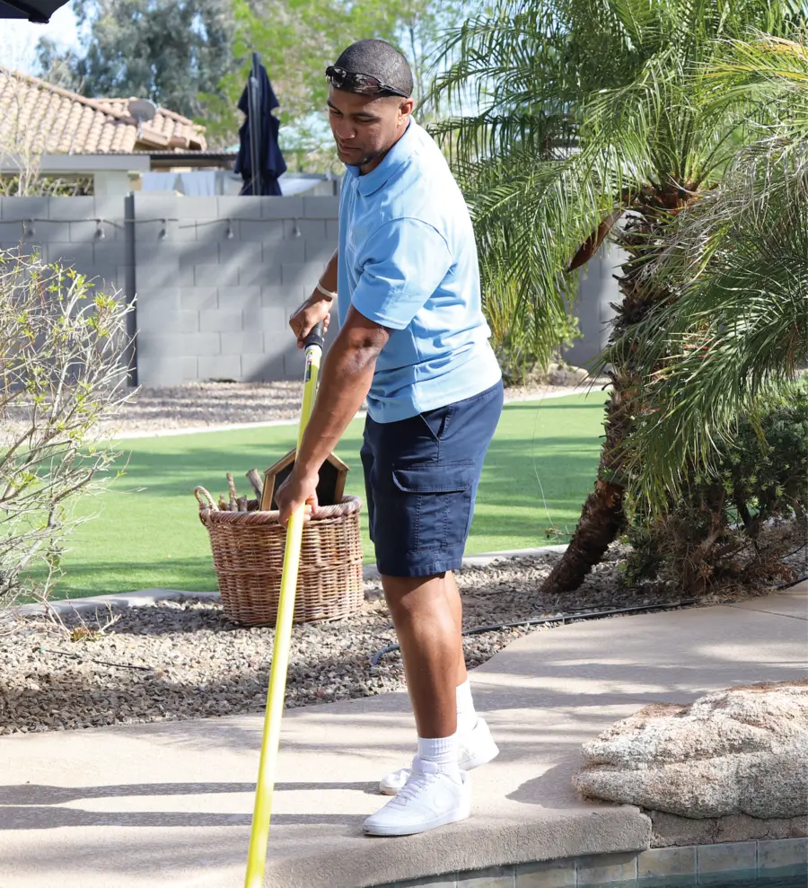 Professional pool technician skimming leaves and debris from a sunny swimming pool with a long-handled net