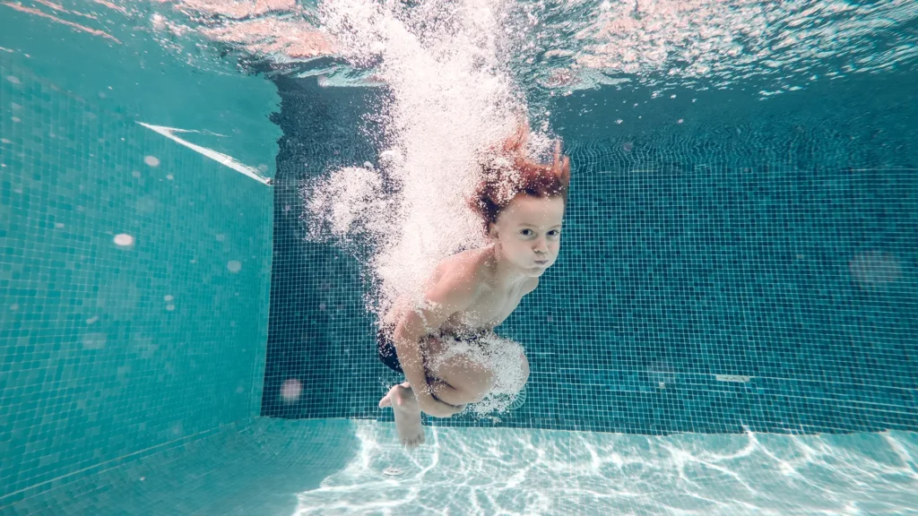 Child swimming underwater in a pool with clear signs of hard water residue on the walls.