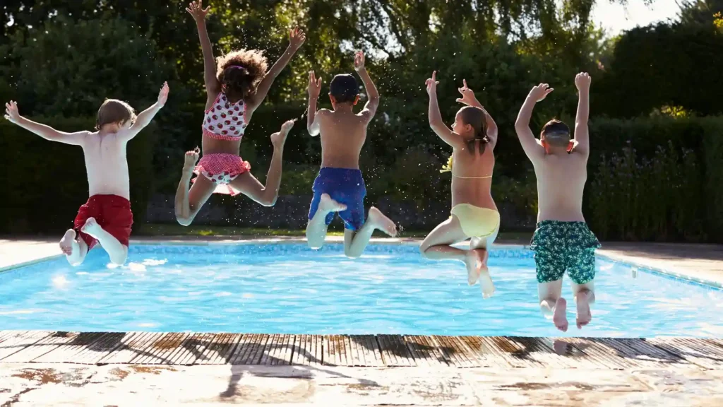 Children safely jumping into a blue pool from a textured anti-slip concrete deck