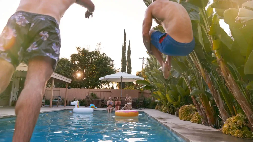 A diverse group of happy adults celebrating by jumping feet-first into the clear blue water of their new backyard swimming pool