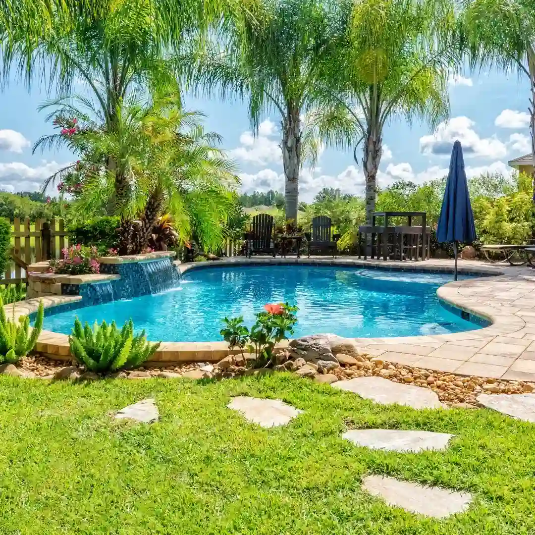 A beautiful swimming pool under bright sunshine, surrounded by lush green grass, with crystal clear blue water and sparkling blue tiles