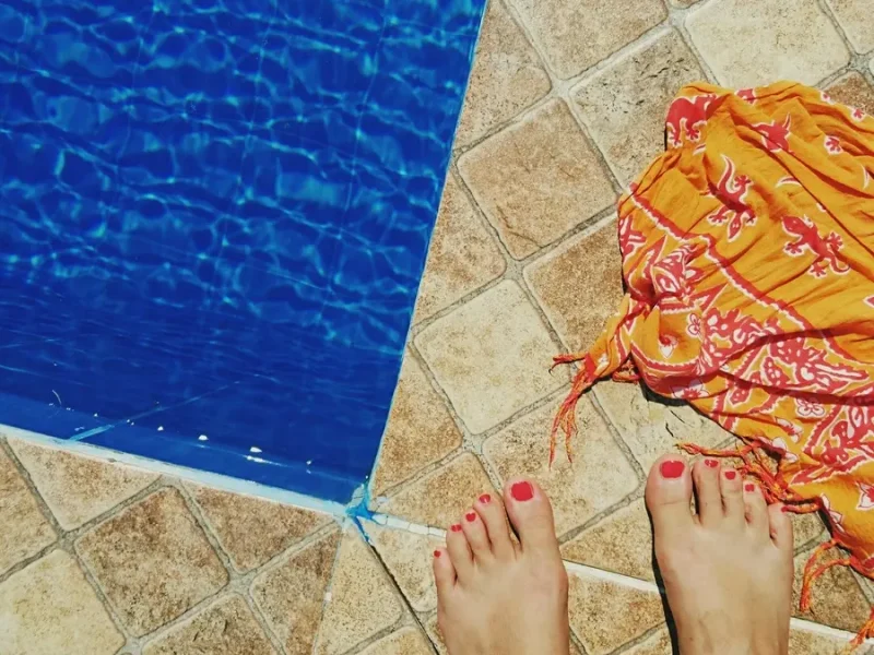 Girl dipping her feet in sparkling pool water while sitting on the pool edge enjoying summer