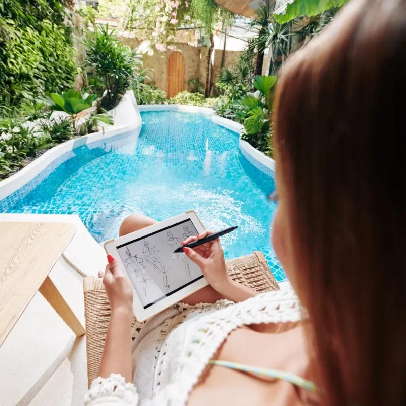 A young girl sketching a pool design on a tablet while standing near a modern swimming pool