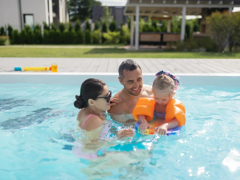 A mom and dad gently teaching their young daughter to swim in a pool