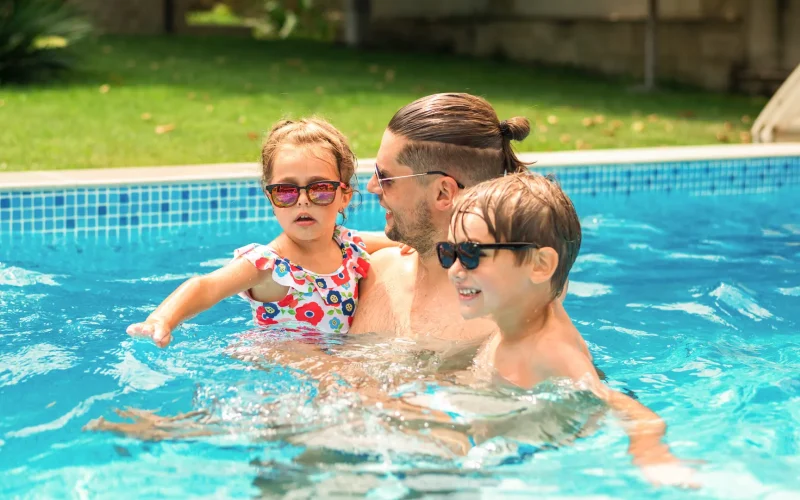 Dad teaching his sons how to swim in their clean, safe pool, maintained by Amenity Pool Services