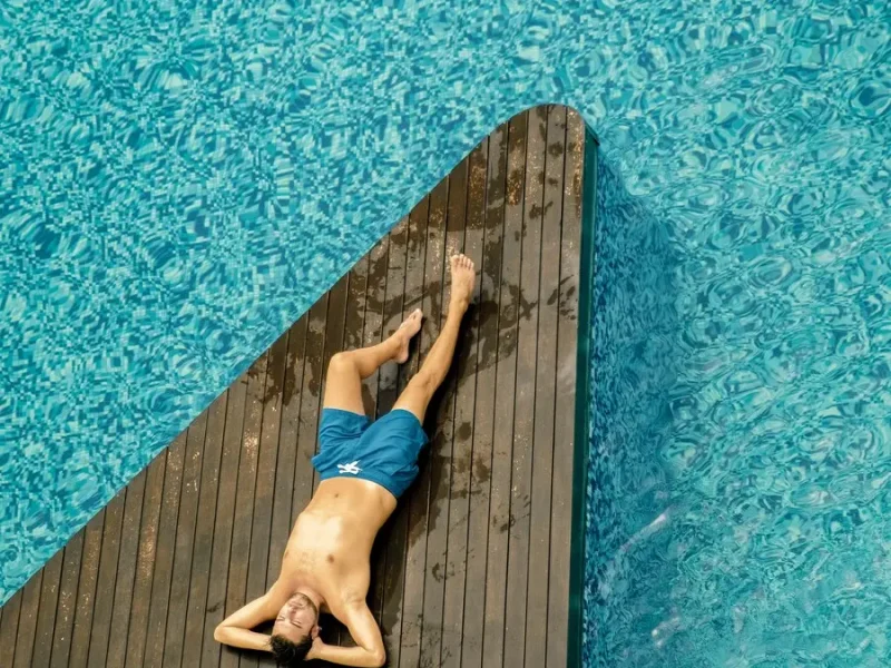 Aerial drone view of a man relaxing on the edge of a swimming pool
