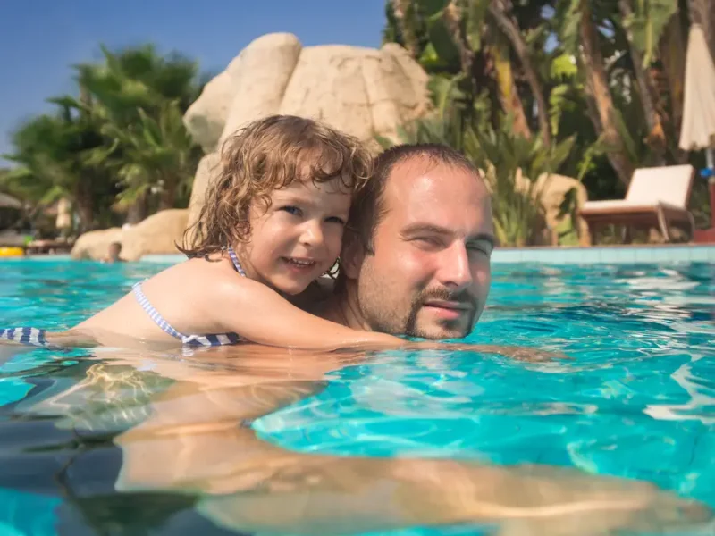 Father and son swimming near natural stone waterfall in luxury pool