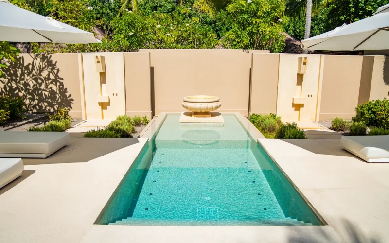 Luxury backyard pool with decorative fountain jets, roman stairs, and crystal-clear turquoise water for resort-like vibes