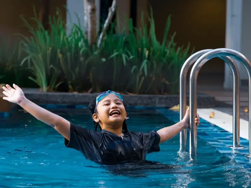 Little kid exiting the pool using silver accessibility handrails