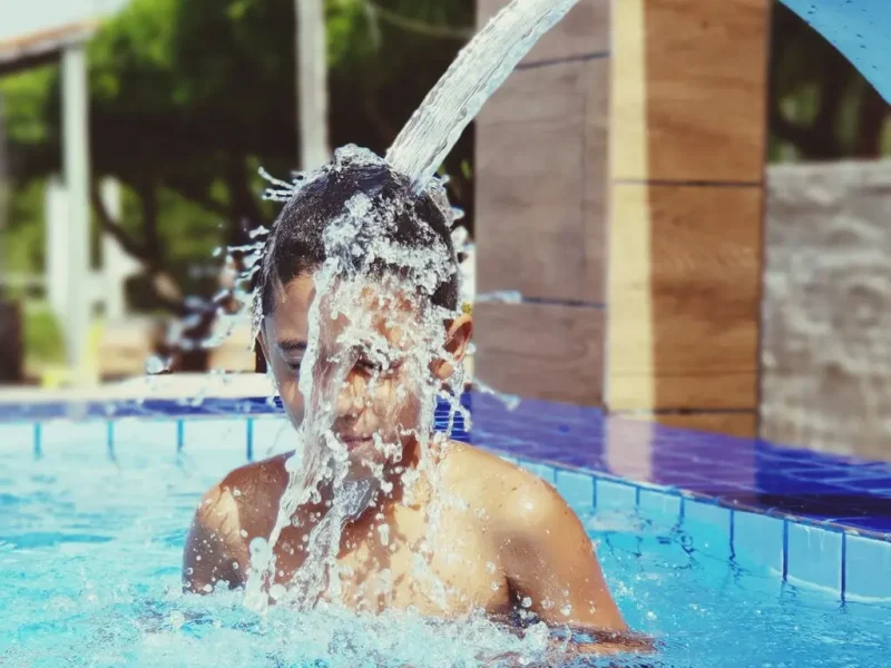 Kid playing in the pool under water fountain